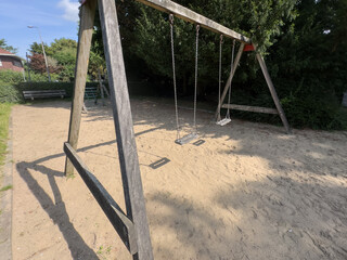 Empty swings on a playground surrounded by lush greenery, symbolizing the end of children's holidays and the return to school routines