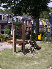 Playground structure with slide and climbing frame in a sunny park, surrounded by residential...