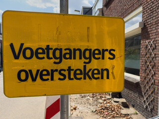 Bright yellow pedestrian crossing sign stands prominently against a brick wall, emphasizing safety...