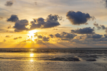 Obraz premium Golden sunset illuminating clouds over calm sea at low tide