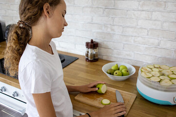 Girl preparing apples for drying in a bright kitchen on a sunny afternoon, showcasing healthy...