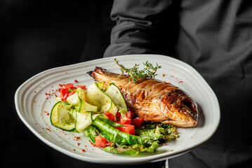 Whole roasted fish with thyme, served on a white plate with fresh zucchini, tomatoes, and greens....