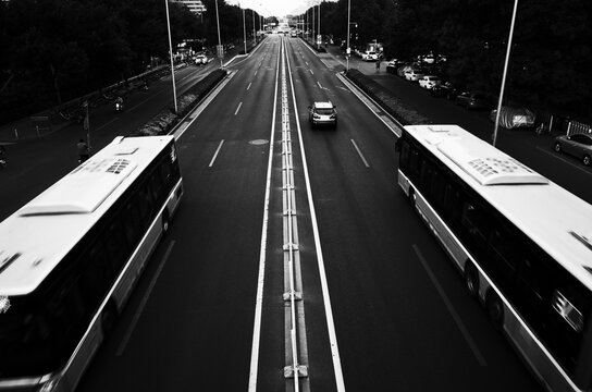 Fototapeta A monochrome photo of a city road in Beijing, featuring two buses moving in opposite lanes. Captured with a strong symmetrical composition and vanishing point perspective. Suitable for editorial 