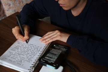 a woman prepares for an exam, takes notes in a notebook or workbook, uses artificial intelligence on a smartphone
