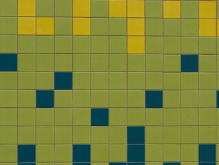 Wall covered with square tiles in different colors, green, yellow and dark blue