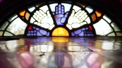 Stained glass window featuring hand symbols and a sun-like shape, reflected on a shiny surface. - Powered by Adobe