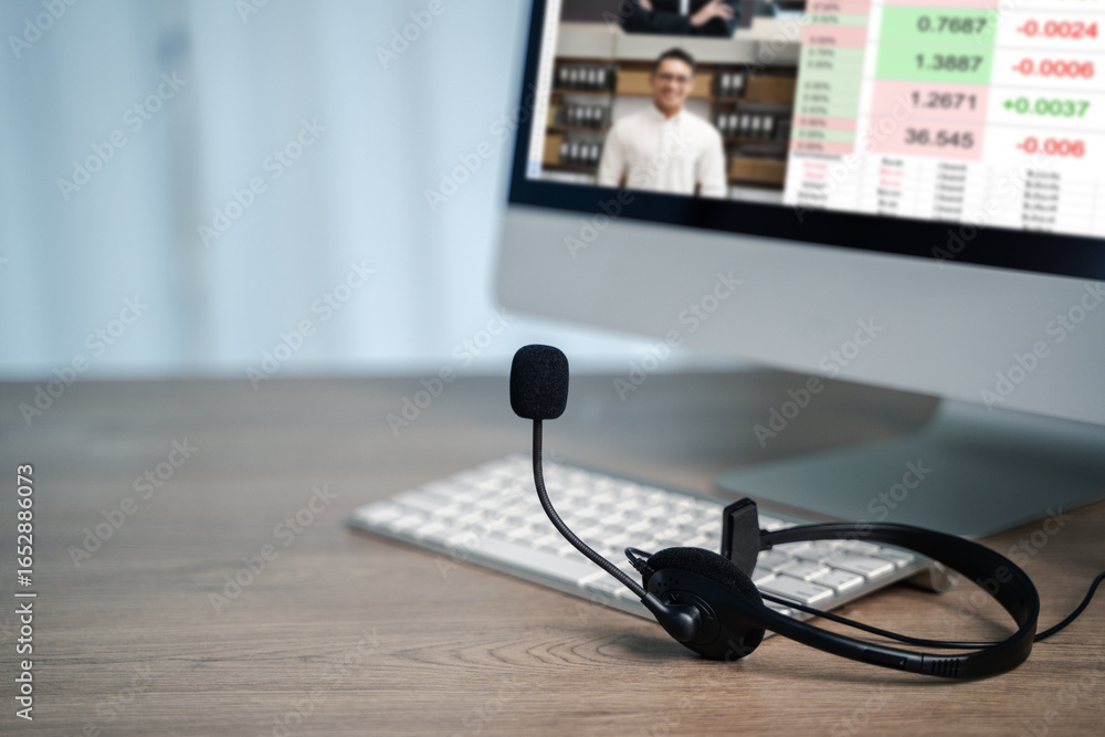Poster work from home setup with headset on desk, showing person in online video conference on desktop moni