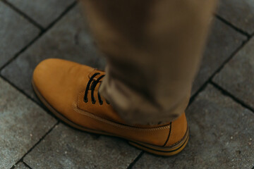 Close-up of beige boot and pant leg stepping on gray paved street. Urban footwear, autumn style, outdoor walk, city fashion, comfort, and modern lifestyle