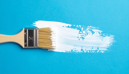 Brush with white paint and brushstroke on blue background. Abstract composition. Top view.
