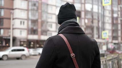 Handsome man wearing black coat and brown leather bag walking down on the city, drinking coffee paper takeaway cup with mobile phone. Stylish bearded middle-aged male using smartphone at urban street - Powered by Adobe