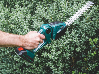 Attractive man, work clothes and hedge trimmer. Close up, outdoors. Labor and employment concept