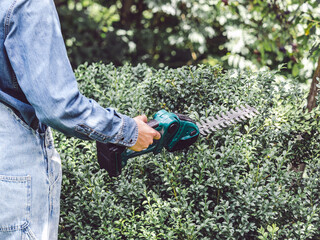 Cute woman, work clothes and hedge trimmer. Close up, outdoors. Labor and employment concept