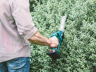 Attractive man, work clothes and hedge trimmer. Close up, outdoors. Labor and employment concept