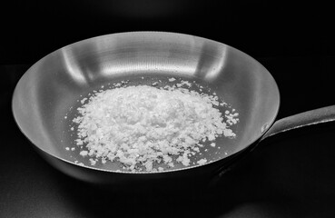 salt flakes in a fry pan, on black background. Black and white Image