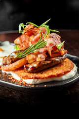 Close-up of crispy bacon, grilled mushrooms, and hash brown on creamy sauce, garnished with herbs and pepper flakes. Gourmet breakfast or brunch dish