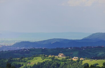 A sweeping panorama reveals green hills dotted with houses in a Romanian landscape. Distant...