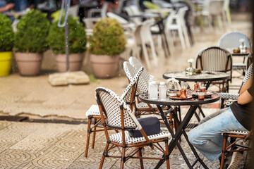 Outdoor café scene during rainfall with traditional coffee pots and glasses on the table. A person sits in wet clothes, symbolizing culture, everyday life, and rainy atmosphere