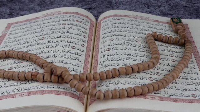 Oom in Opened page Holy Quran tasbih or rosary beads on top. Isolated background.