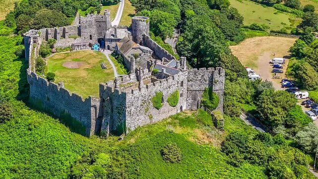 A close in rotating aerial view around the old Norman castle ruins at the seaside resort of Manorbier, South Wales in summertime