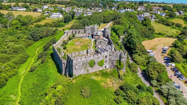 A rising aerial view looking over the old Norman castle ruins at the seaside resort of Manorbier, South Wales in summertime