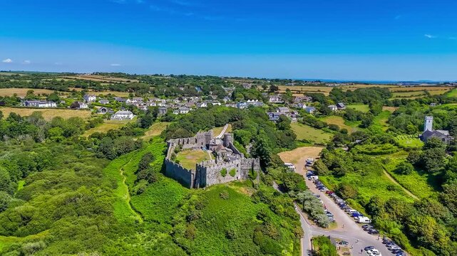 A distant rotating aerial view around the old Norman castle ruins at the seaside resort of Manorbier, South Wales in summertime