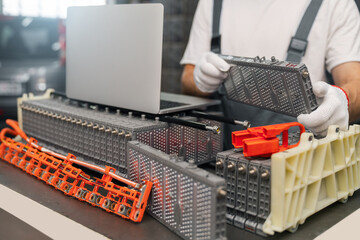 Serviceman repairs electric battery pack of hybrid car using laptop