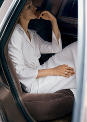 A thoughtful young woman in a white outfit sitting in a car's interior, in quiet contemplation.
