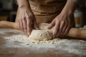 Fototapeta premium Hands skillfully roll out fresh dough on a floured wooden table, preparing ingredients for homemade baked goods. This rustic kitchen scene captures the of traditional baking and culinary craft.