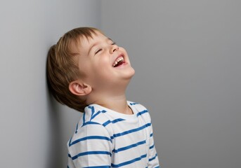 A young boy laughing with his eyes closed, leaning against a wall, wearing a striped tshirt