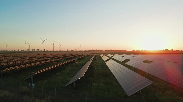 Rows of solar panels and wind turbines in countryside field at sunset. Concept of renewable energy, sustainable technology and clean electricity production
