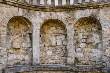Historic stone wall with three recessed arched niches and weathered masonry in a classical garden...