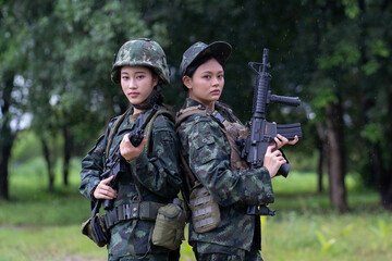 Two soldiers camouflage uniforms stand back to back holding rifles, set against lush, green forest...