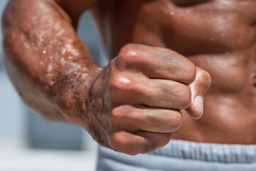 Fototapeta premium Muscular male fist clenched with visible veins and hair on forearm, showing strength and power with blurred torso background in natural light