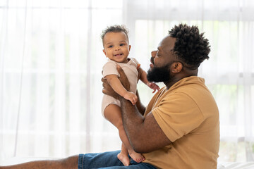 Fototapeta premium Smiling black father holding adorable infant son baby at home. Happy family African American dad bonding with his cute newborn.