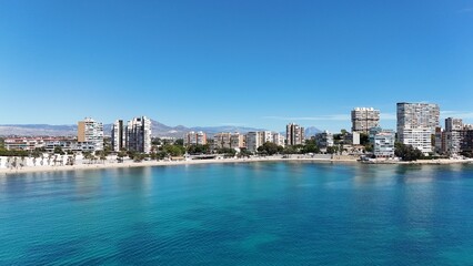 Obraz premium Panoramic view of a coastal city with modern buildings, sandy beach and clear blue sea under a bright sunny sky