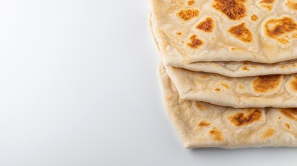 A stack of freshly baked, homemade flatbread sits on a white surface, showcasing its golden brown crust and inviting texture, ready to be enjoyed with a meal.