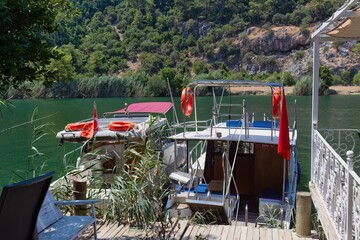 Two boats rest on a wooden dock, flags waving gently. Lush greenery fills the background in Dalyan...