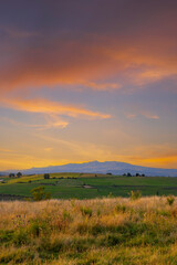 Fototapeta premium Colorful sunset illuminating green fields and distant mountains in Auvergne Rhone Alpes, France