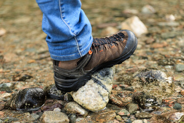 closeup of a foot wearing tracking boots stepping on a stone in a stream,  Norway summer, hiking experience