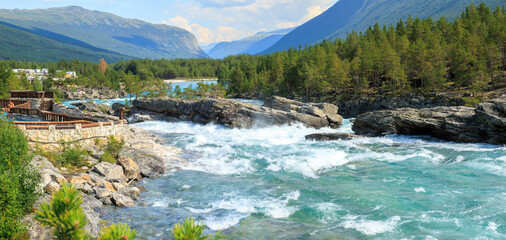 overlook the sapphire blue D&oslash;nfoss river running against the giant rock with forest and moutain in summer Norway, E6 road landscape