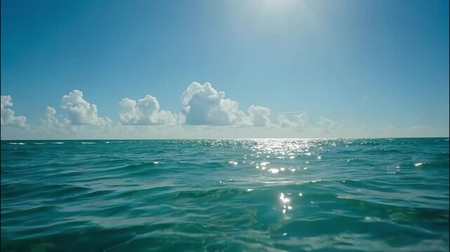 Calm tropical ocean waves under the midday sun, horizon line filled with billowing white clouds, crystal-clear turquoise waters with light reflections.