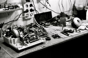 A cluttered workbench in black and white, filled with electronics and tools, symbolizing the...