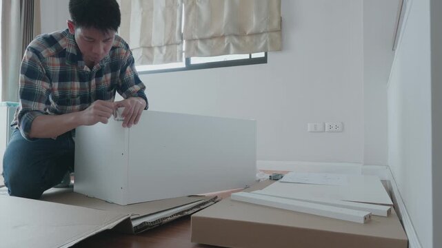 A person is focused on assembling a piece of flat-pack furniture in a well-lit room. The workspace features cardboard packaging and tools, showcasing the DIY process and the importance of home organiz