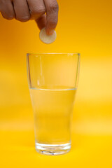 A person holding a vitamin c tablet and a glass of water on an orange background.