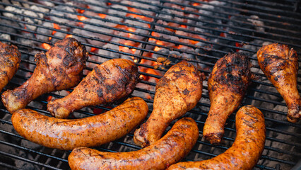 chicken drumsticks and seasoned sausages sizzling on a hot charcoal grill