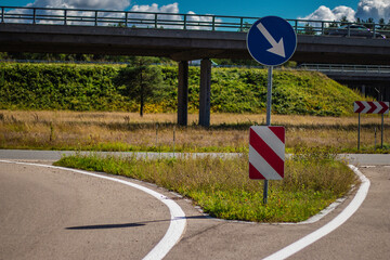A curved road at a highway junction featuring directional traffic signs, including a blue arrow...