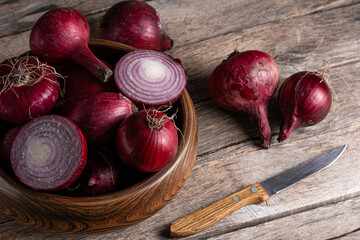 Red onion in wooden bowl on wooden background with knife.