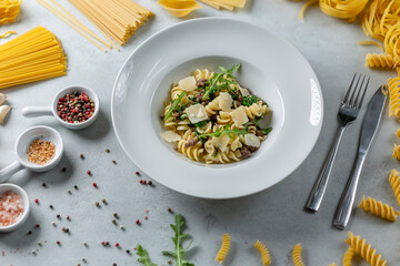 White plate with fusilli pasta, parmesan, arugula and minced meat, surrounded by ingredients on...