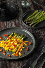 Delicious baked asparagus with melted cheese and bacon bits on a dark plate