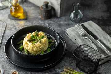 Delicious risotto with green asparagus and grated cheese being served on black plate